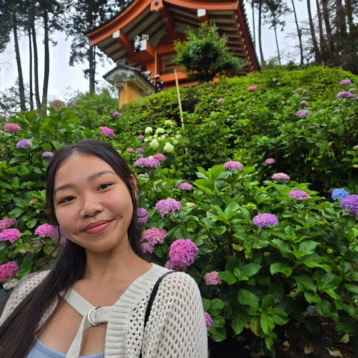 Madeline Ho in front of a garden bush with pink flowers.